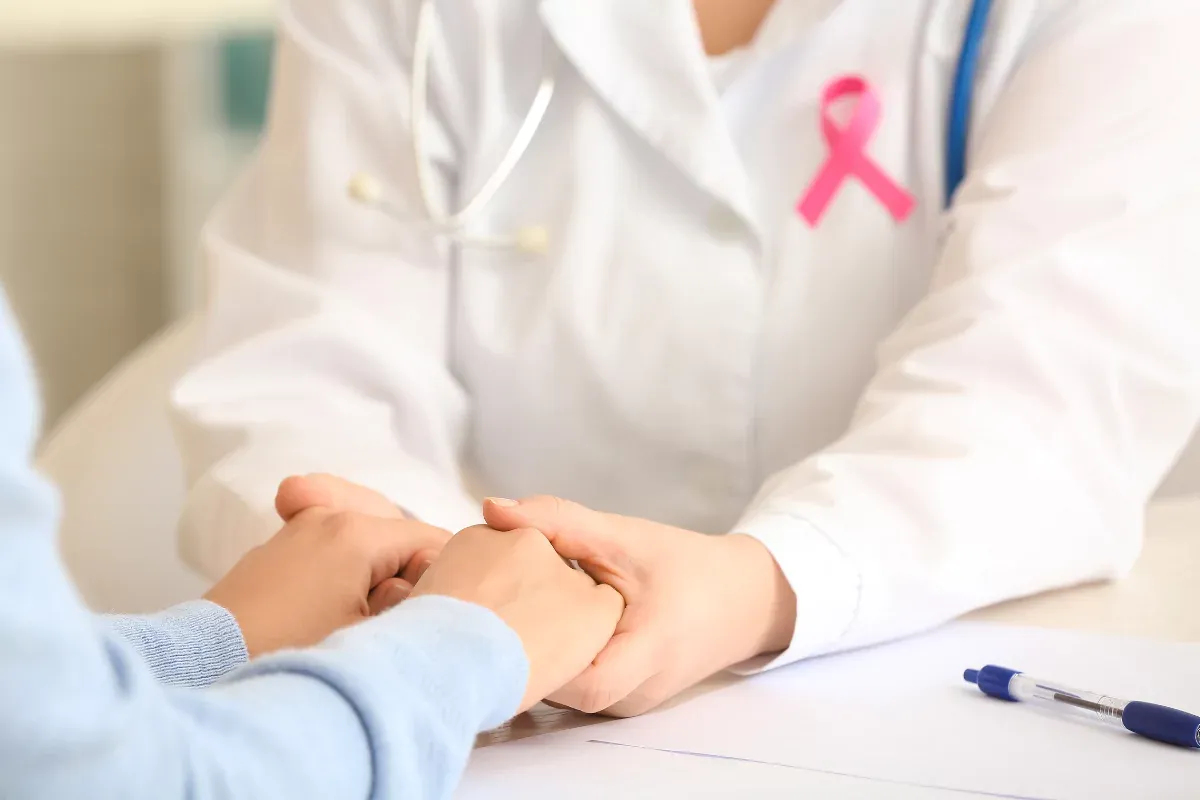 Doctora con lazo rosa sosteniendo las manos de un paciente