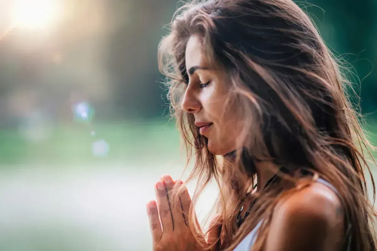 Mujer de perfil, con las manos juntas en señal de oración y meditación.